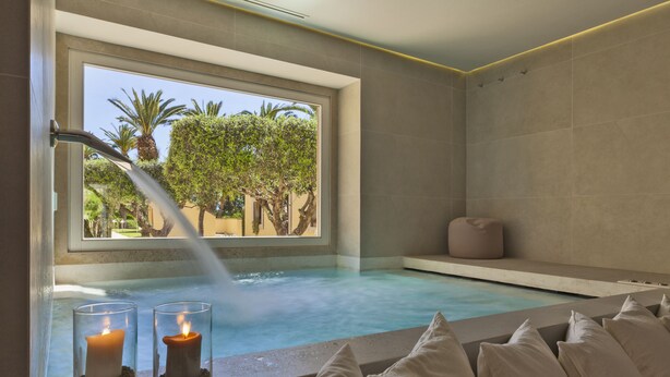 Un cuarto de spa con un amplio ventanal, una bañera de hidromasaje y dos velas.