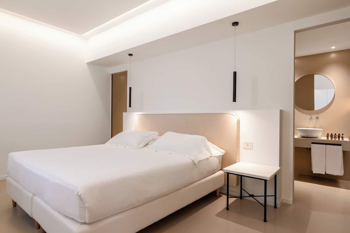 Un dormitorio moderno con una cama grande, mesita de noche y baño con lavabo y espejo.