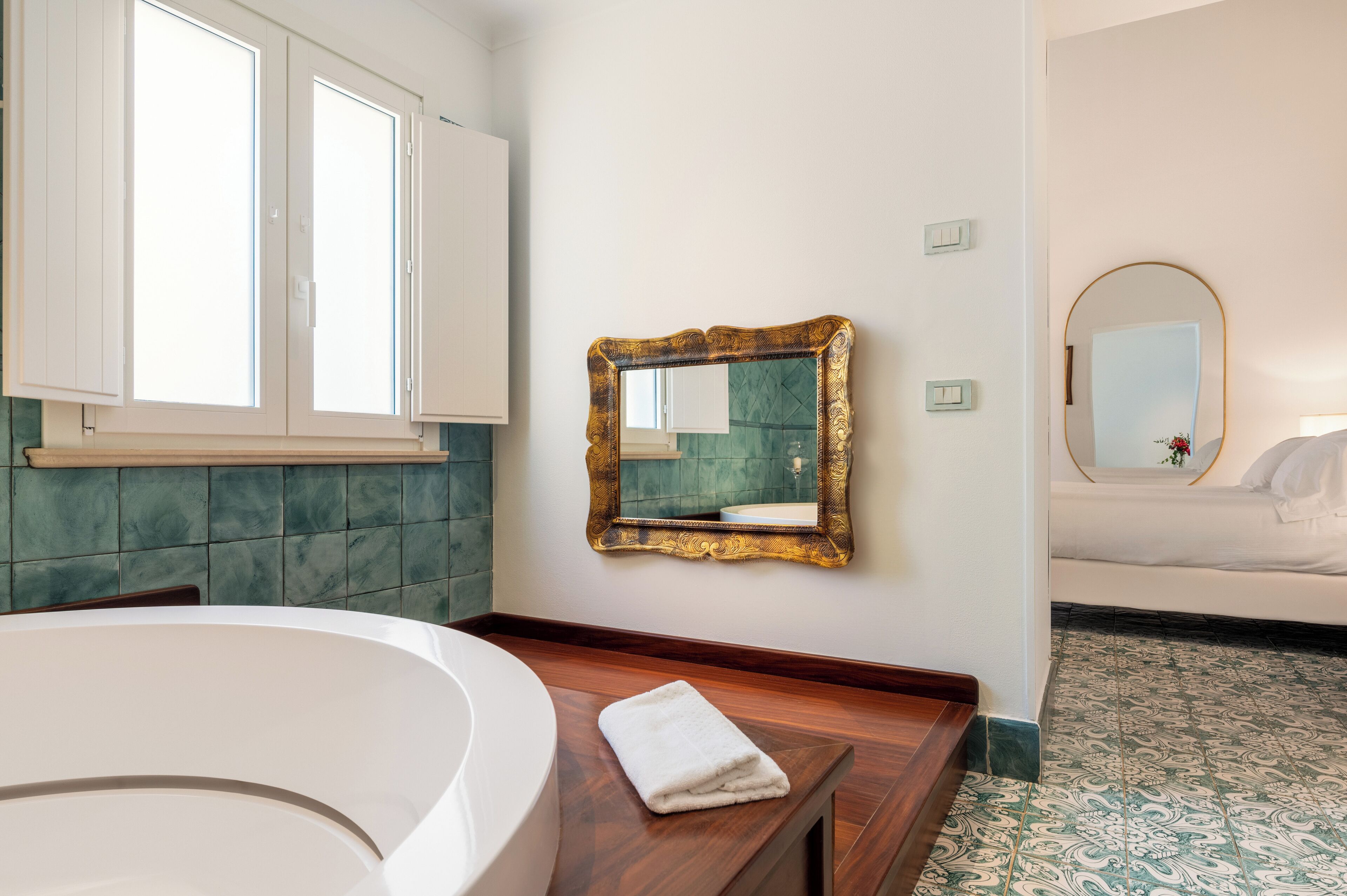 A bathroom with a bathtub, a vanity with a mirror, and a bed with a nightstand.