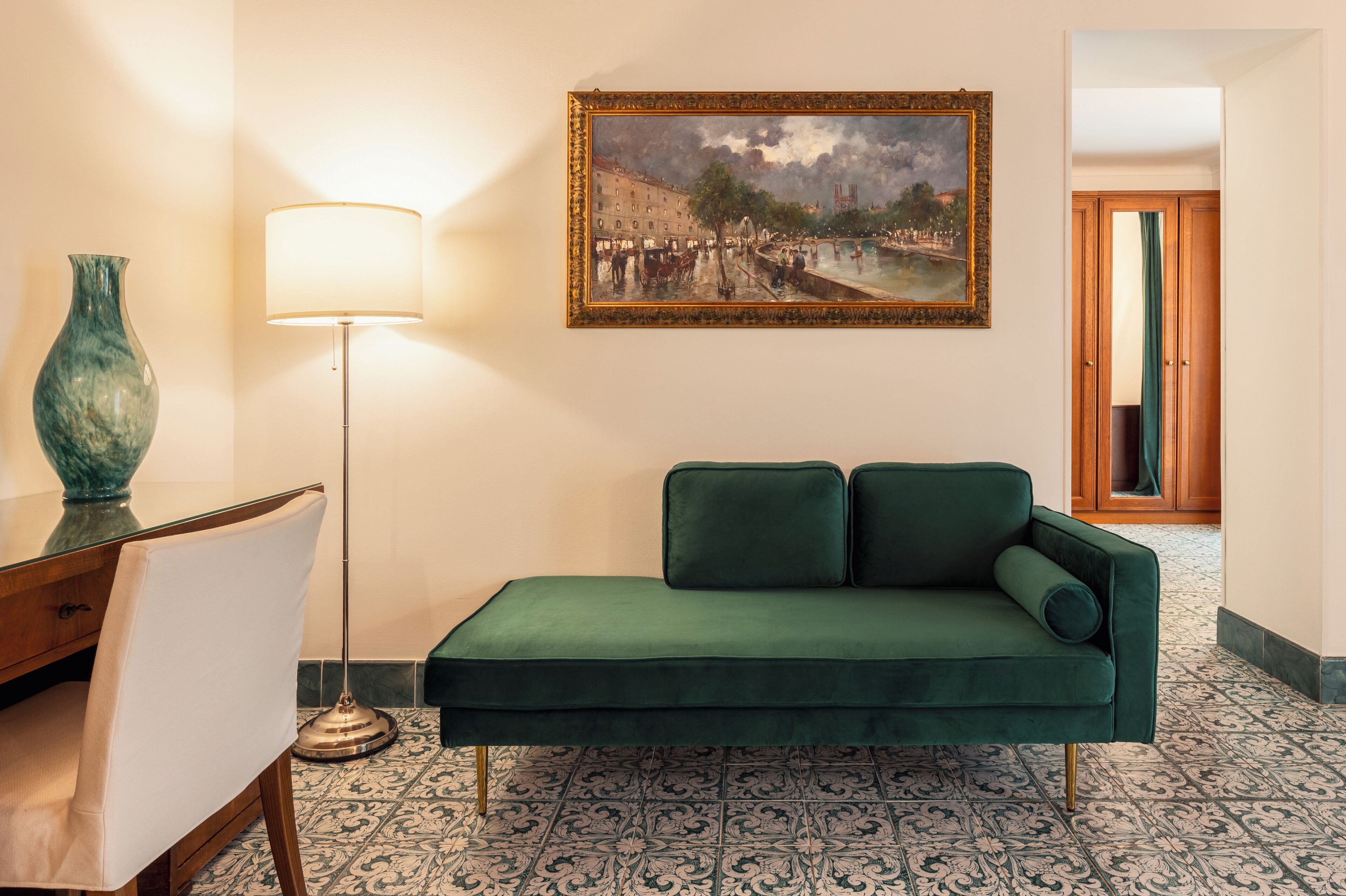 Une pièce avec un canapé vert, une lampe, un tableau et un sol carrelé.