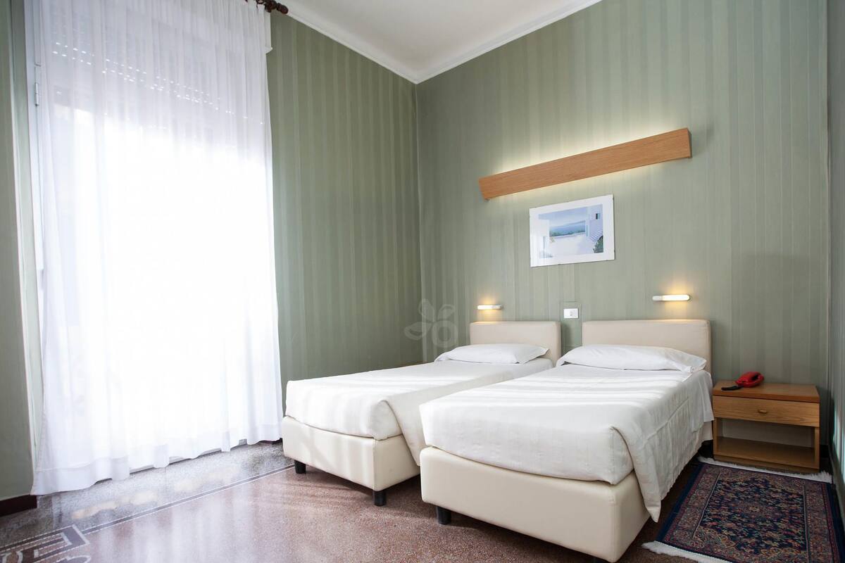 A hotel room with two beds, a nightstand, a small table, a framed picture on the wall, and a patterned rug.