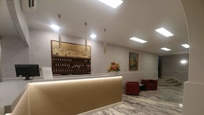 A reception area with a marble floor, a reception desk, a computer monitor, a wall-mounted wine rack, and a staircase in the background. - Hotel Vittoria & Orlandini (Genoa)