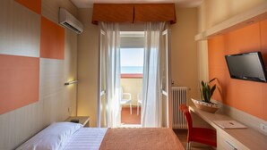 A hotel room with a bed, a desk with a chair, a TV, and a view of the sea through a balcony. - Hotel Regent (Pescara)