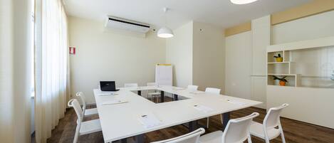 A conference room with a white table, white chairs, a whiteboard, and a white ceiling light.