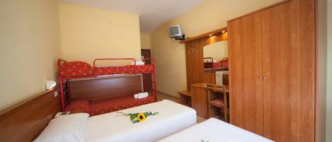 A hotel room with two single beds, a wooden wardrobe, a desk, and a television.