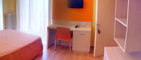 Un dormitorio con una cama, un escritorio con una silla, un televisor montado en la pared y un armario.