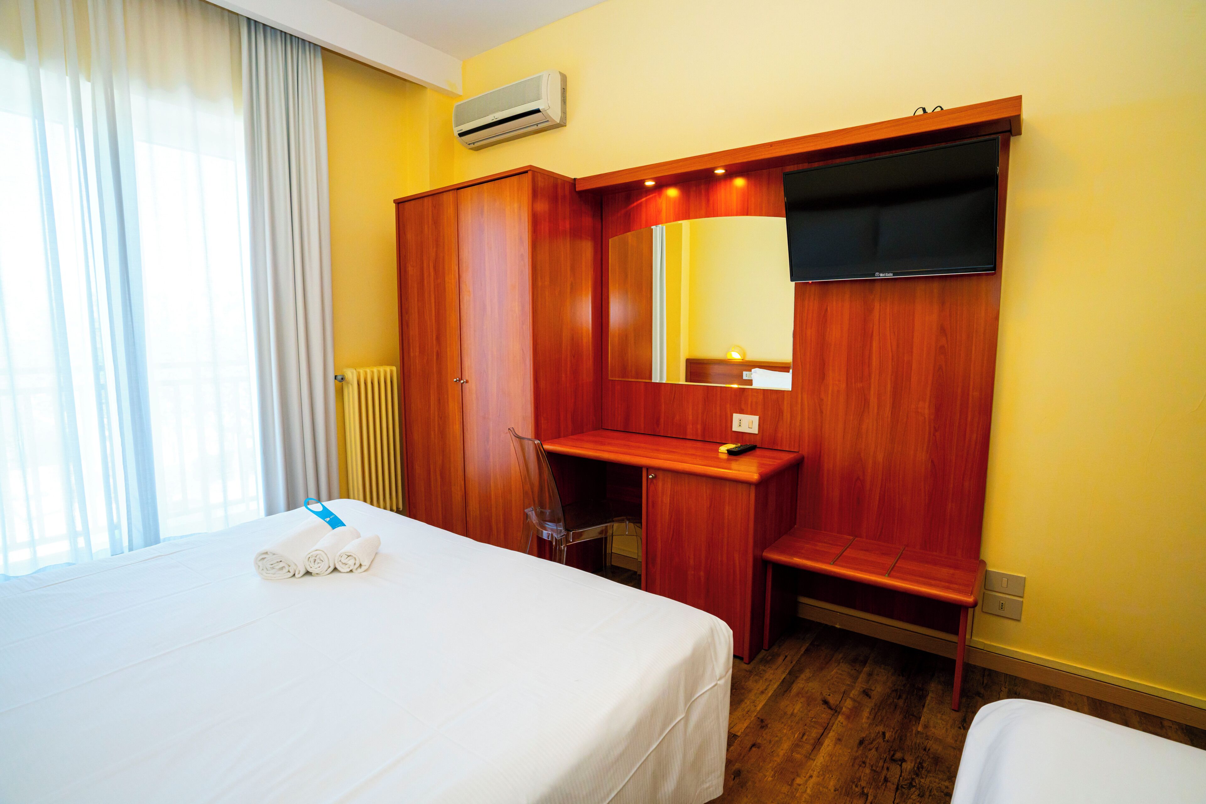 Una habitación de hotel con una cama, un escritorio, un espejo y una ventana con cortinas.