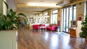 A spacious room with a wooden floor, a red sofa, a white table, and a large window with a view of greenery. - Hotel Regent (Pescara)