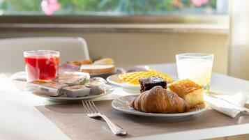 Una mesa de desayuno con cruasanes, gofres y un vaso de jugo.