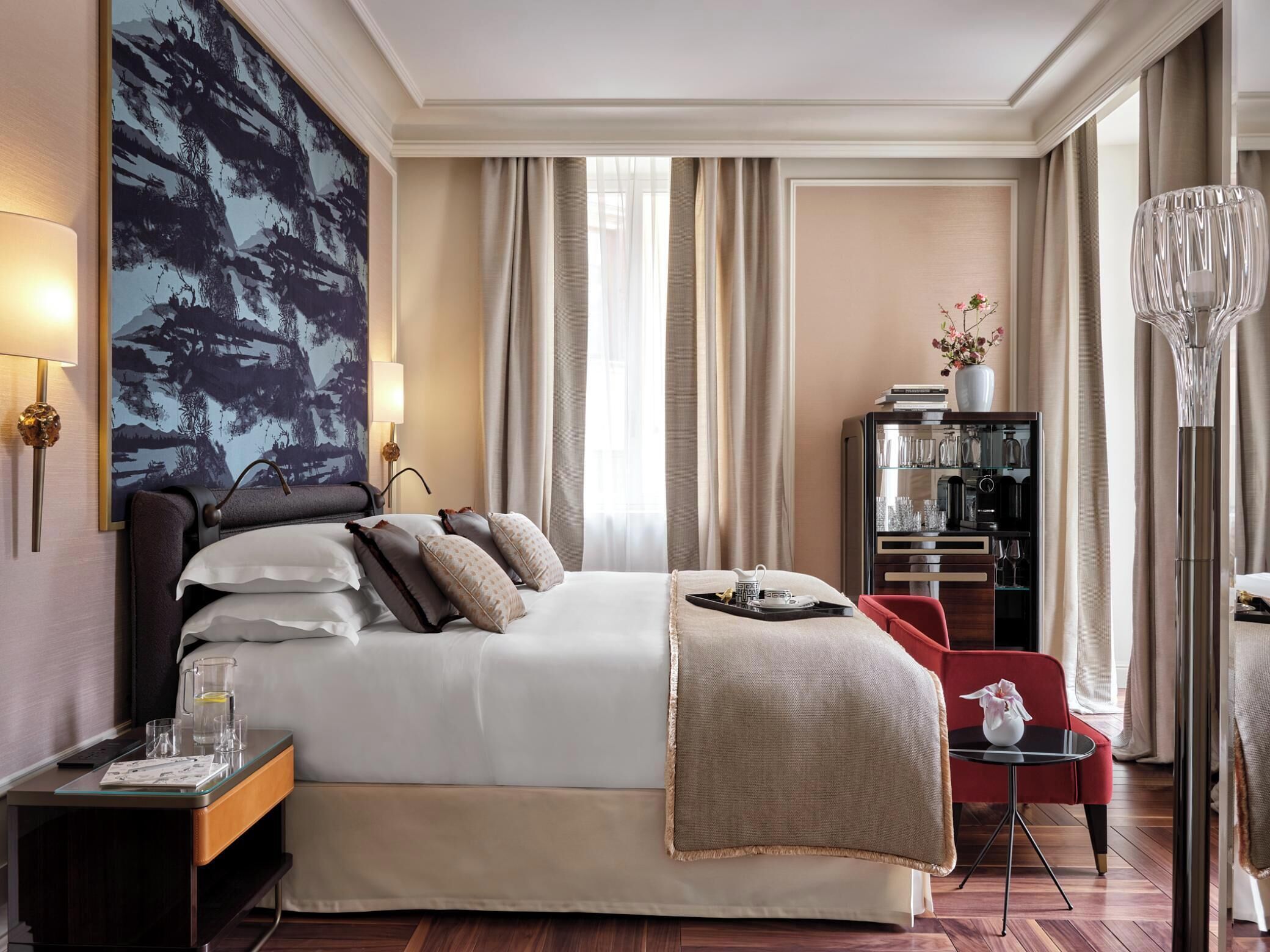 Une chambre d’hôtel avec un grand lit, une table de chevet avec une lampe, une petite table avec un vase et une bibliothèque.