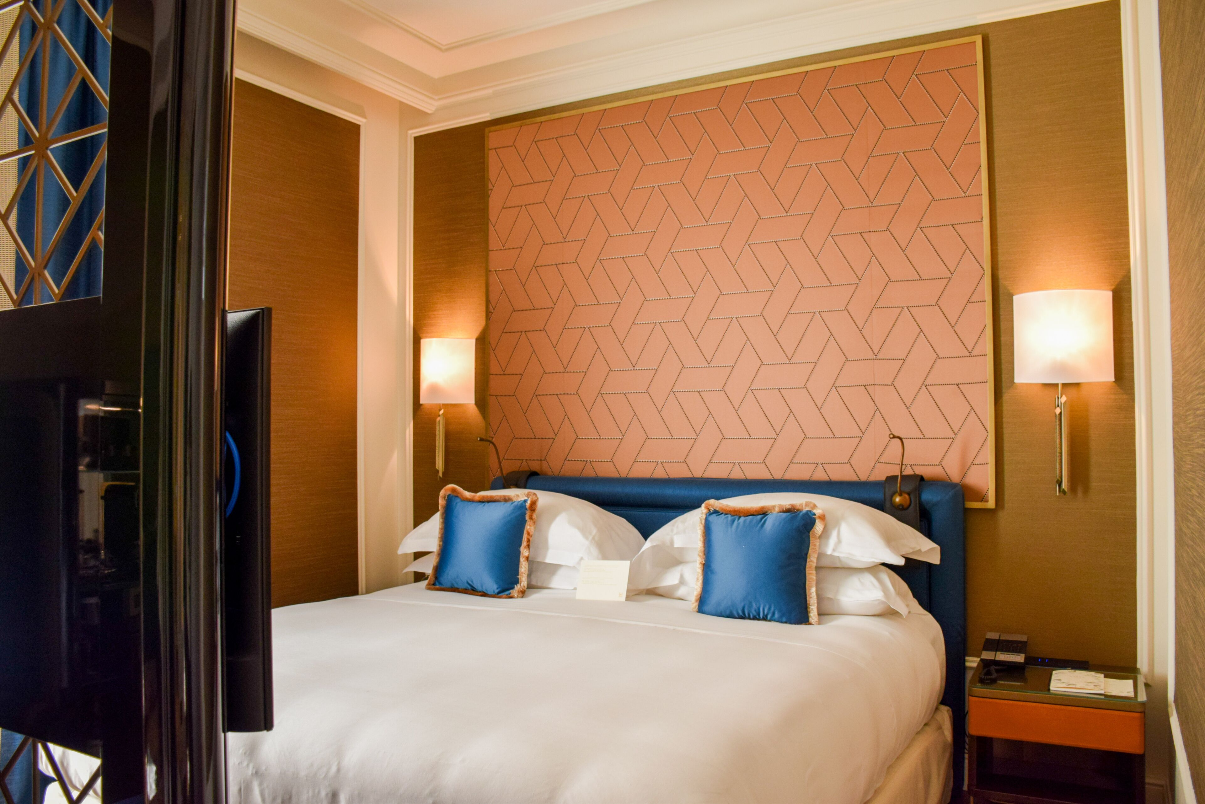 Una camera d'albergo con un letto grande, due lampade sui comodini, una televisione e una parete con motivo geometrico.