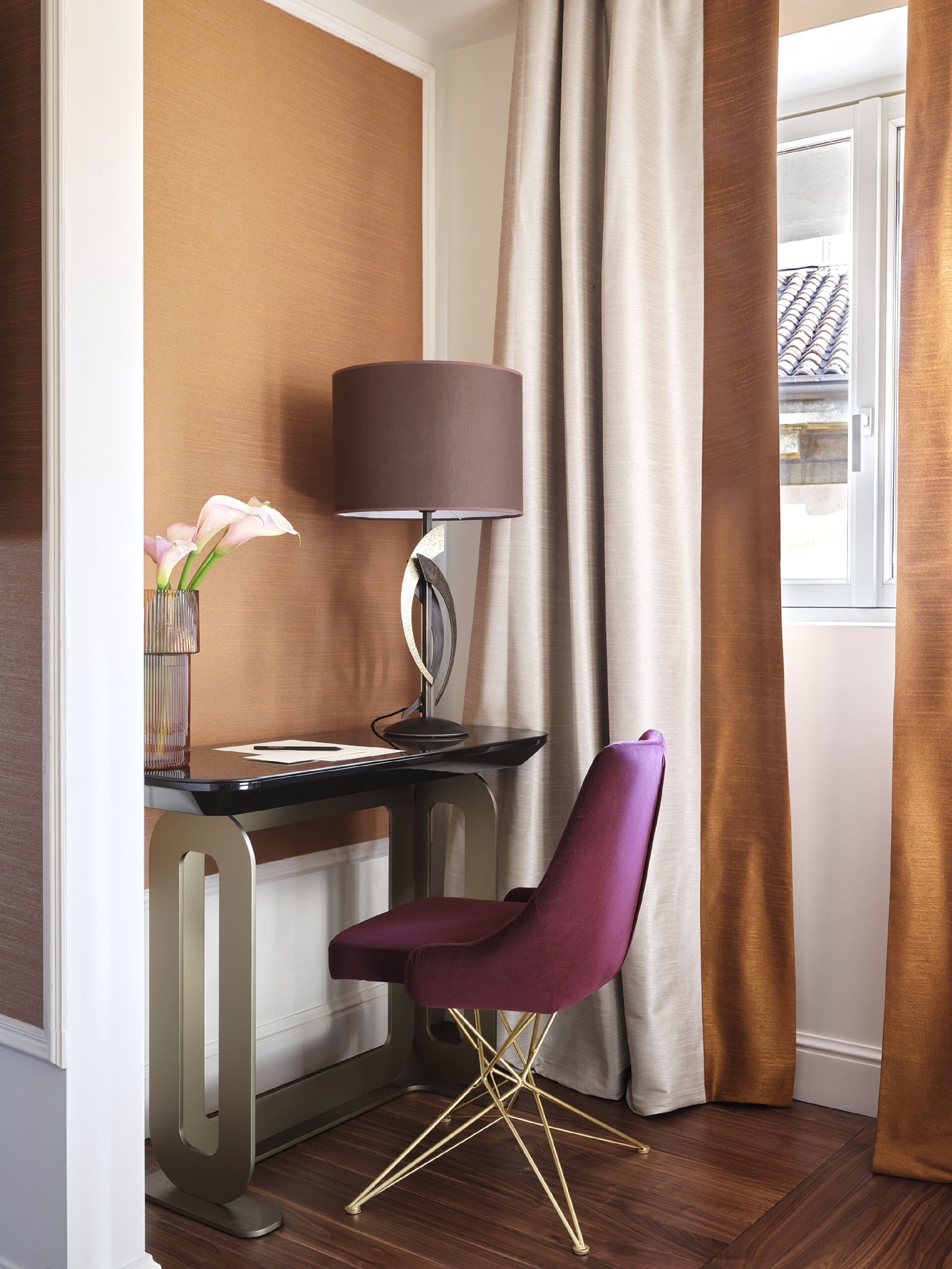 A corner desk with a lamp, a purple chair, and a vase with flowers.
