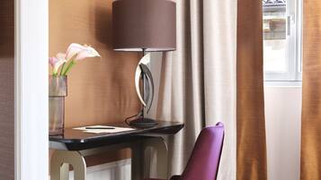 A corner desk with a lamp, a purple chair, and a vase with flowers.
