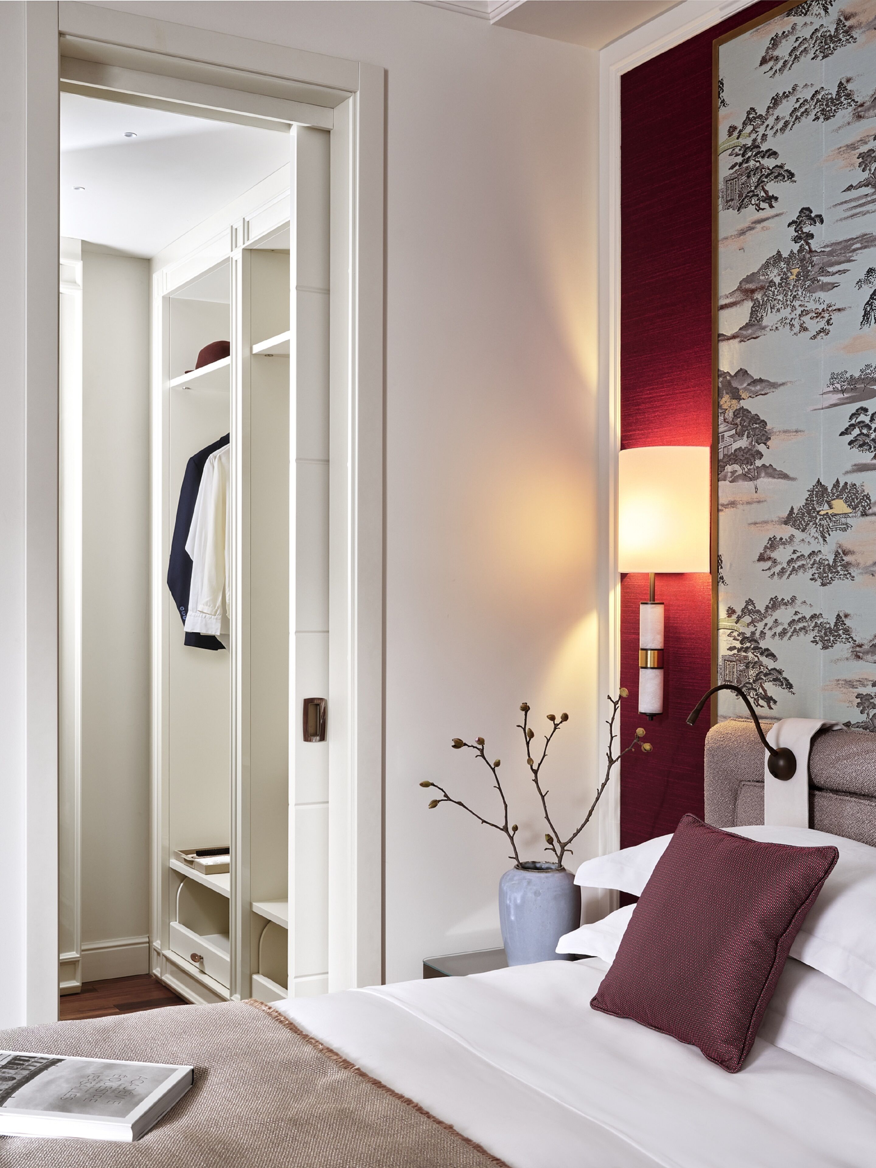 A hotel room with a bed, bedside table, lamp, and a view of a wardrobe.