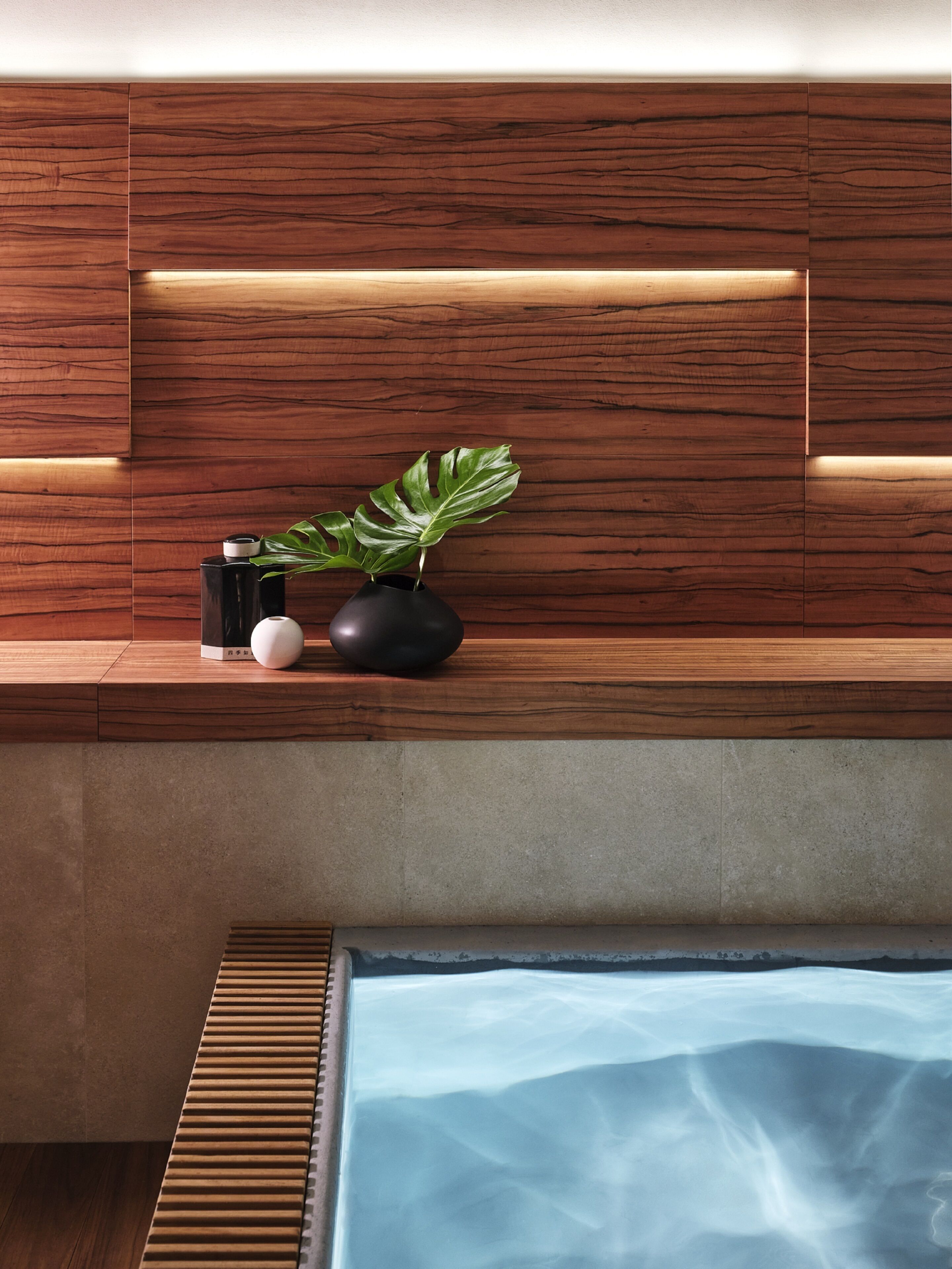 A modern bathroom with a wooden vanity, a black vase with a plant, and a blue bathtub.
