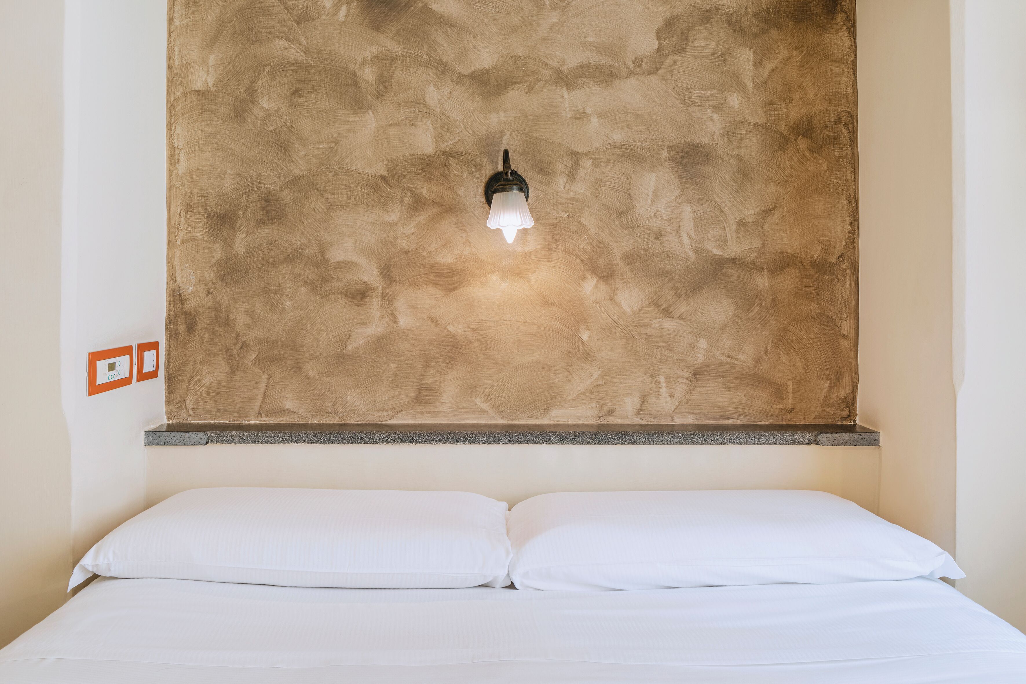 A bed with white linens and a wall-mounted light fixture.