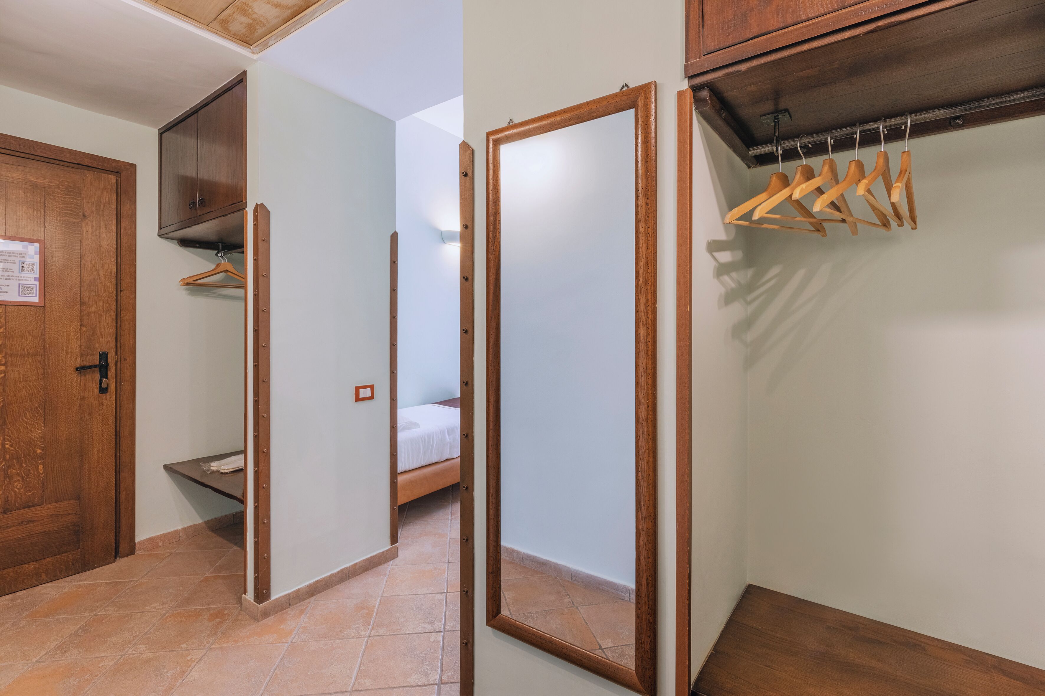 A room with a wooden door, a bed, a wardrobe, and a coat rack.