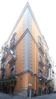 Un edificio ad angolo con facciata beige, diversi balconi e una insegna che indica che si tratta di un hotel.