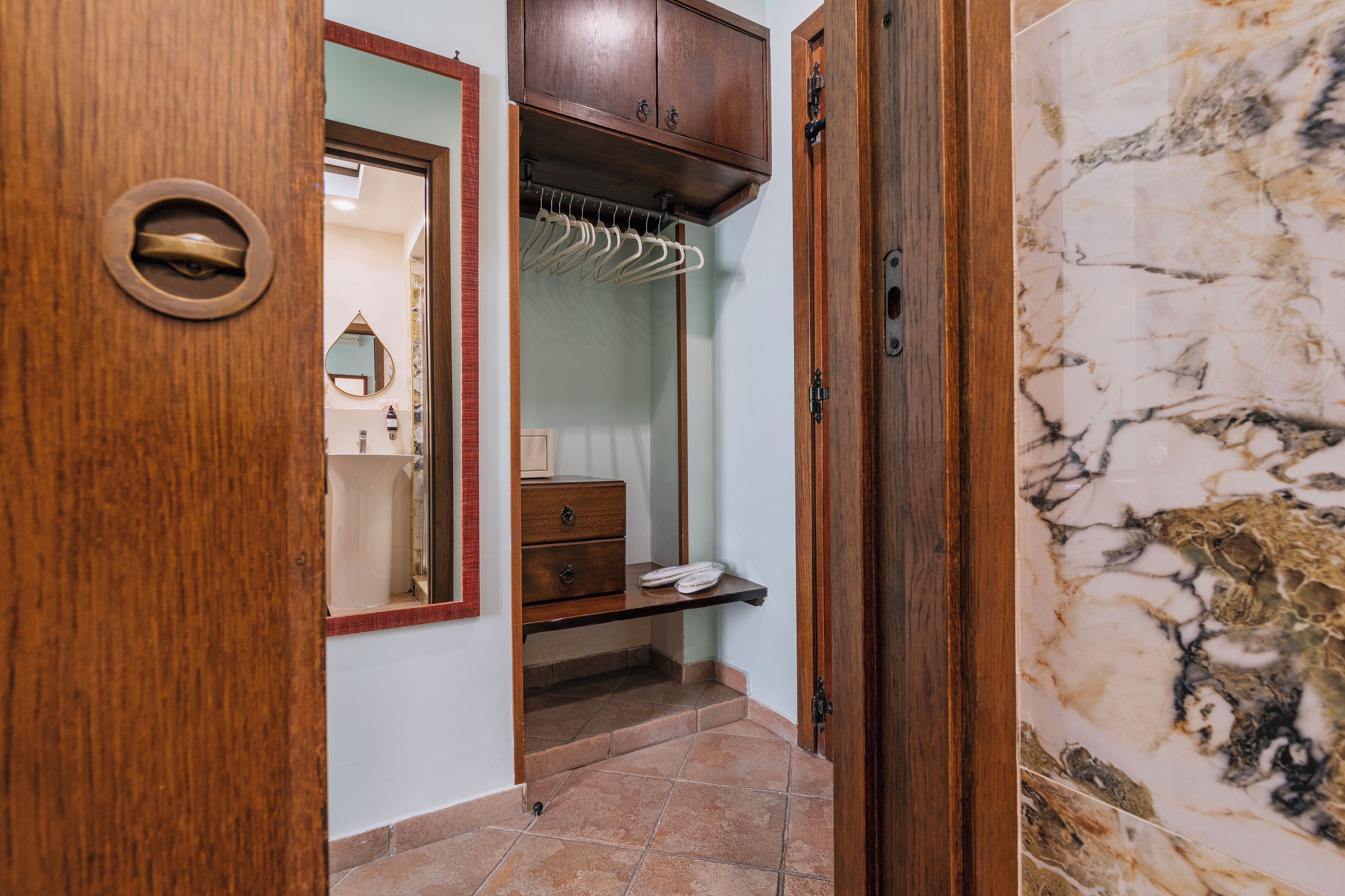 Une porte en bois avec une poignée en laiton, une armoire en bois avec un miroir, et un sol carrelé.
