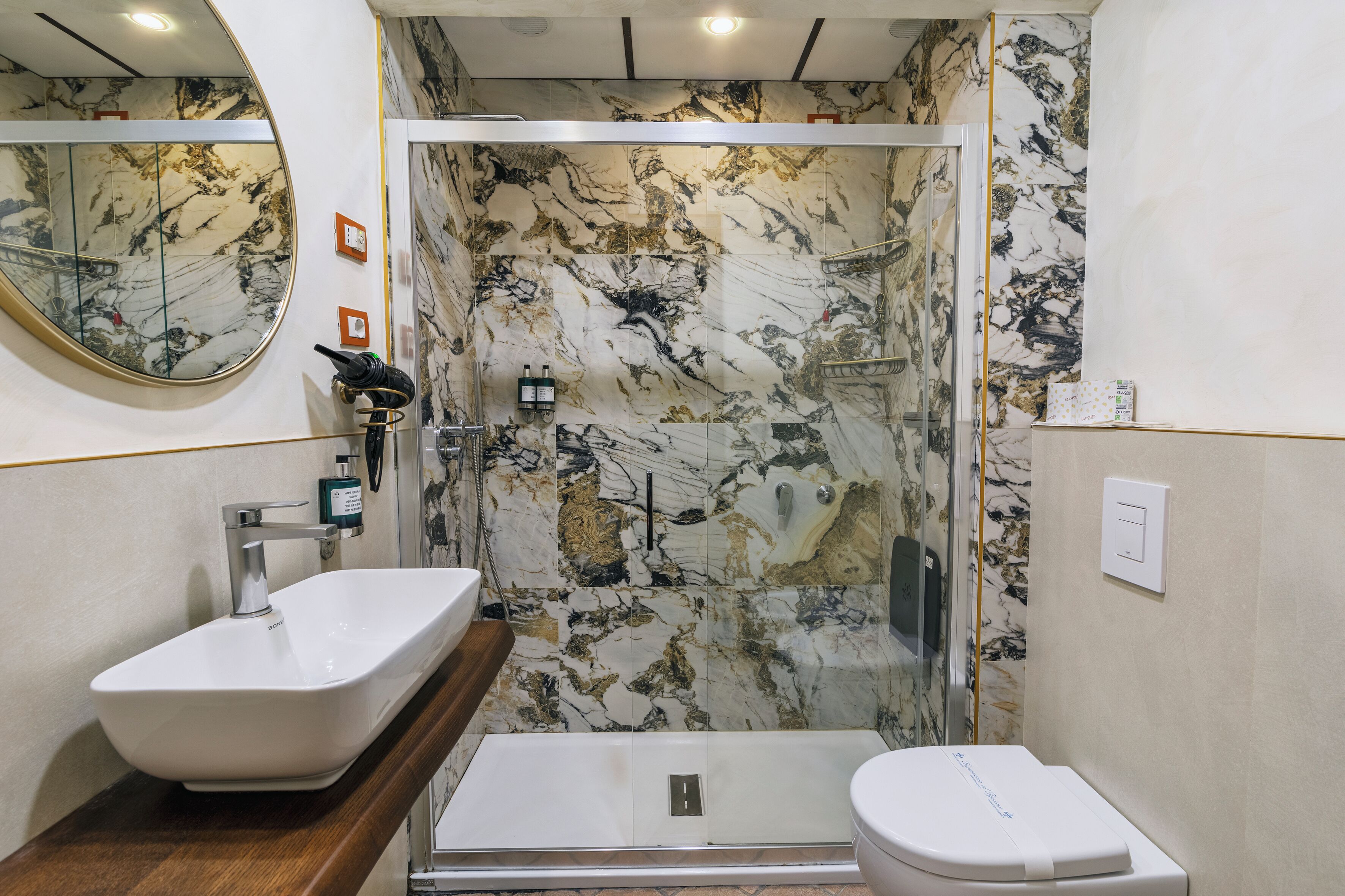 A bathroom with a marble backsplash, a sink, a toilet, and a shower area.