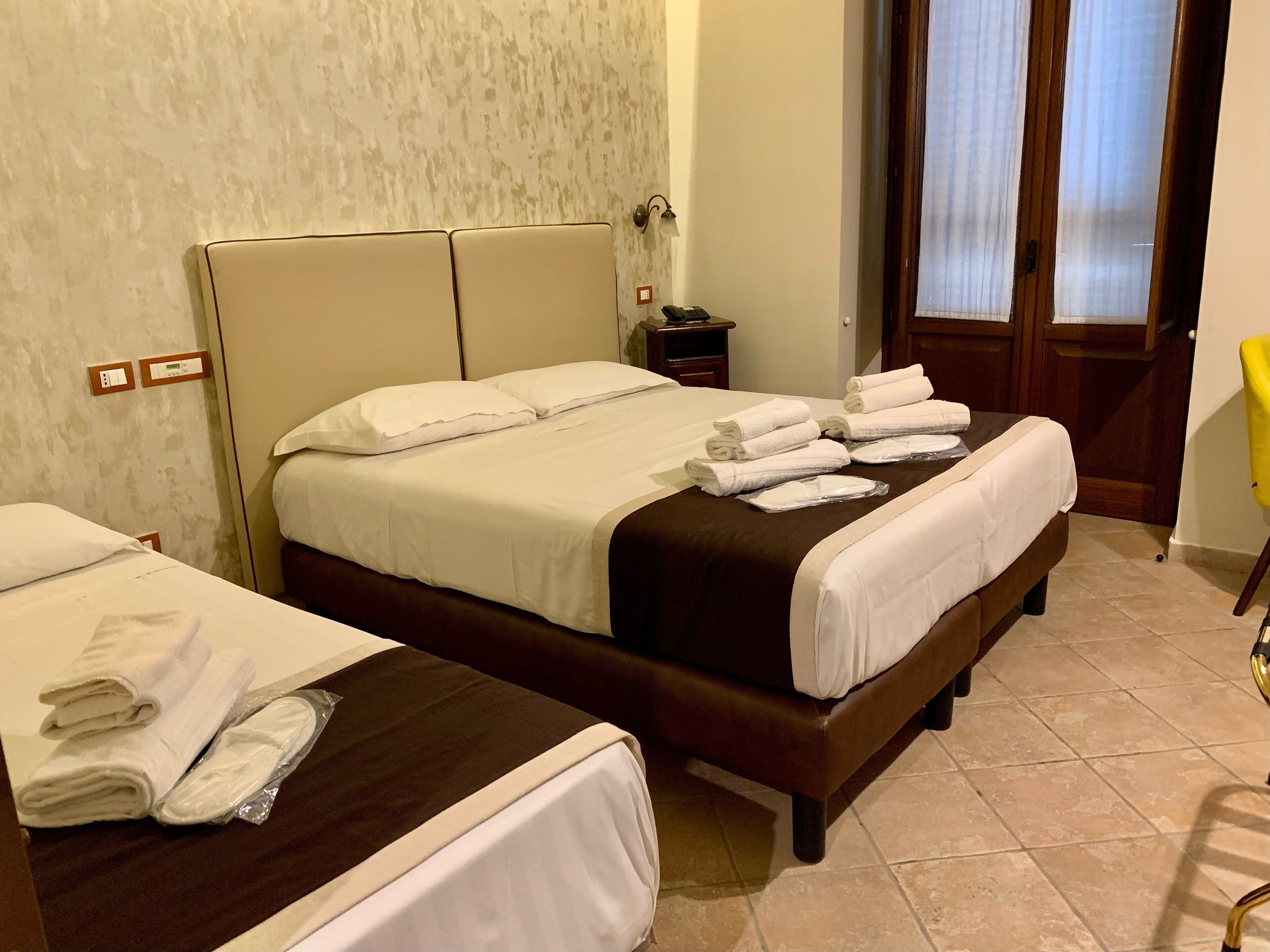 A hotel room with two beds, a nightstand, a chair, and a bathroom door.