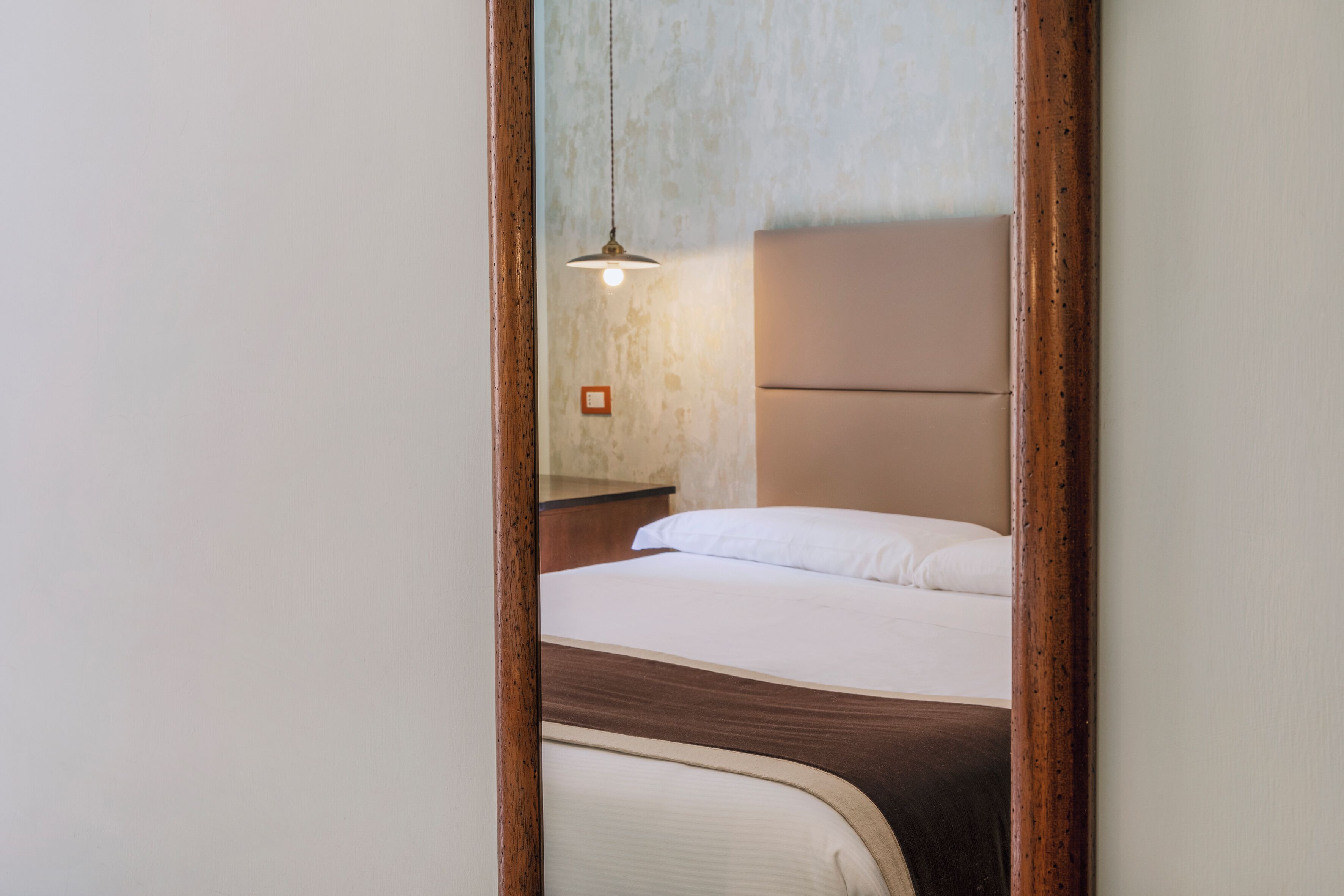 A bedroom with a bed, a hanging light fixture, and a wooden headboard.
