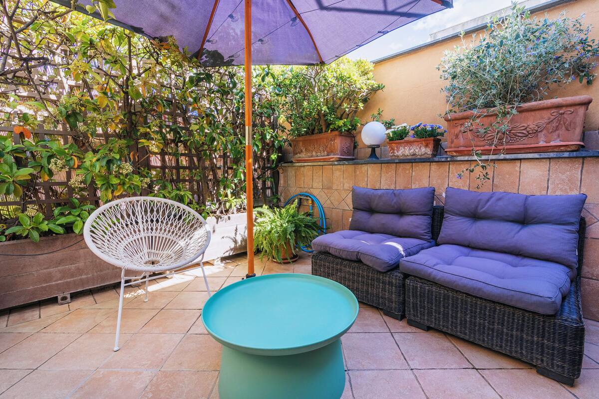 Un patio con un sofá de mimbre, una silla blanca y una mesa verde.