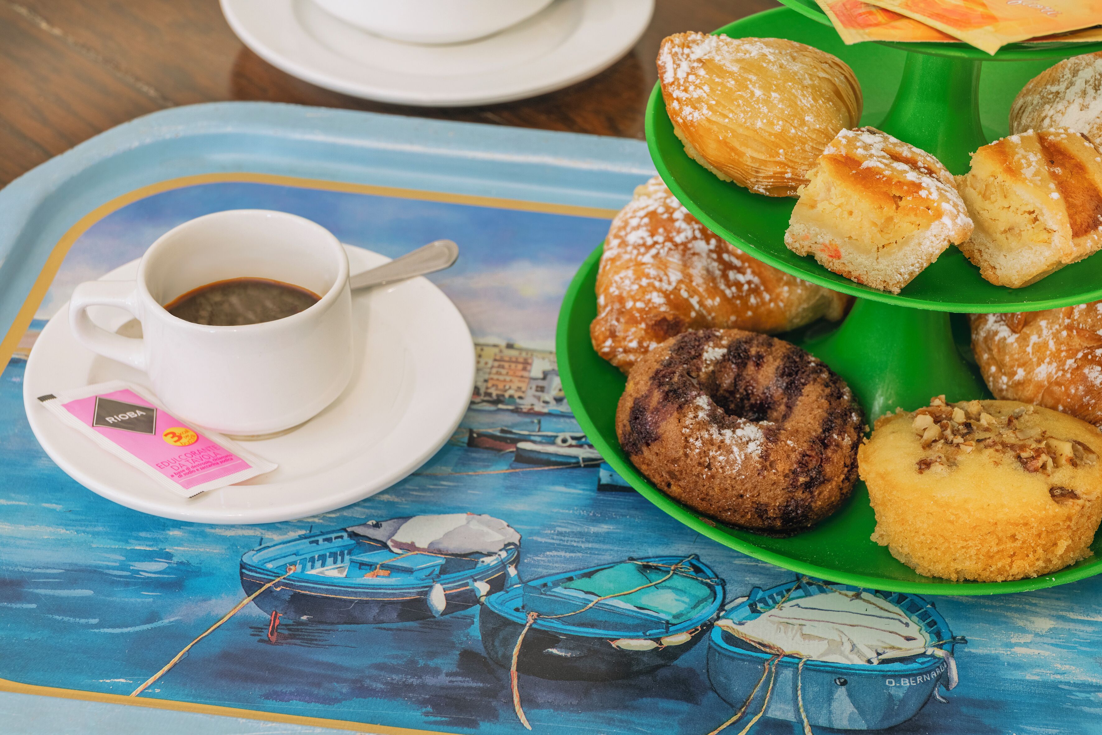 A tray with pastries and a cup of coffee on a table with a boat painting.