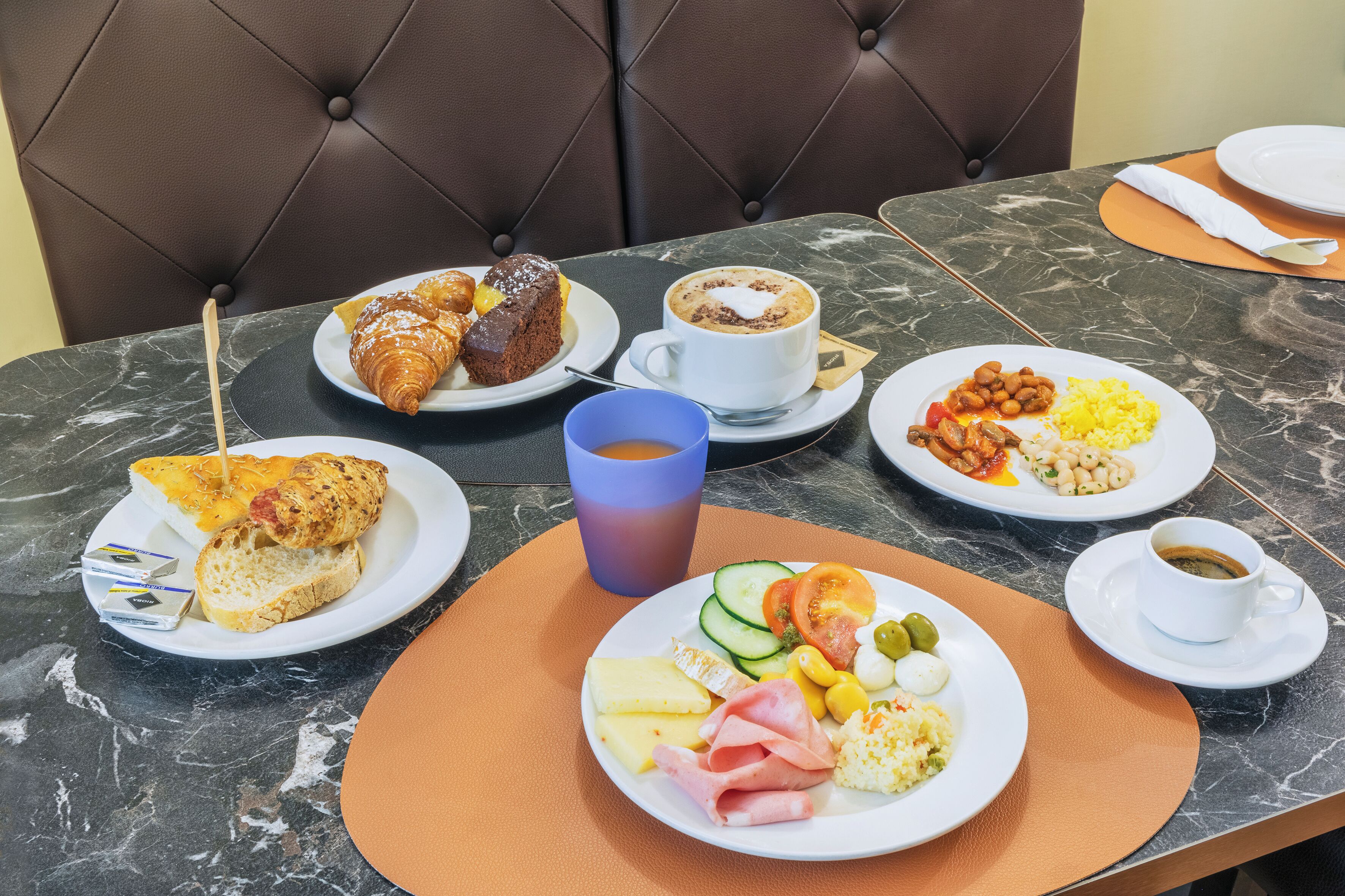 Una mesa de desayuno con croissants, una taza de café y platos de huevos, jamón y verduras.