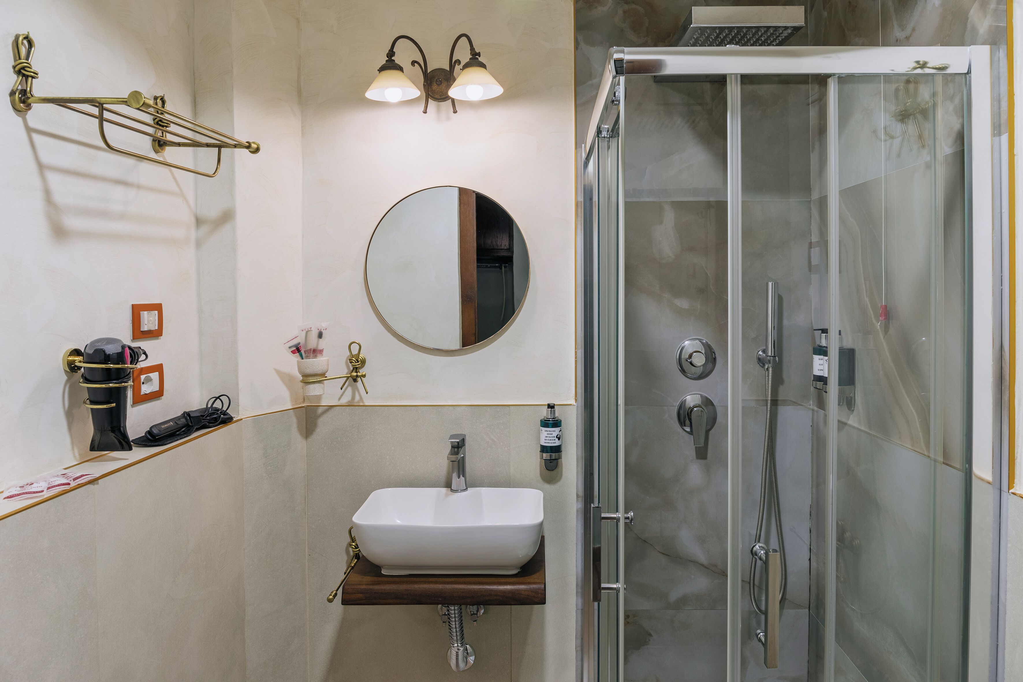 A bathroom with a white sink, a round mirror, a shower with a glass door, and a towel rack.