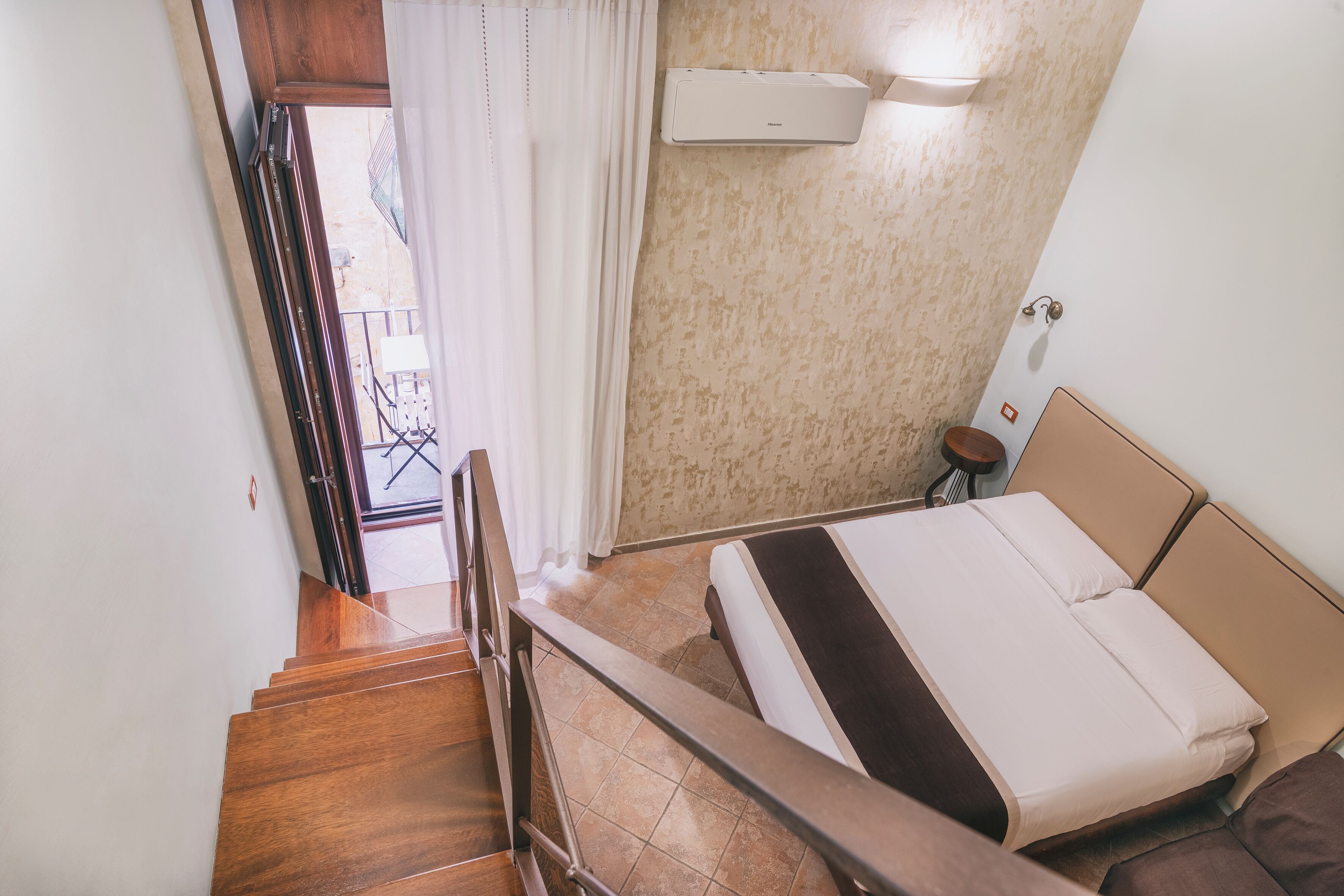 A bedroom with a bed, a window with curtains, a wooden staircase, and an air conditioning unit.