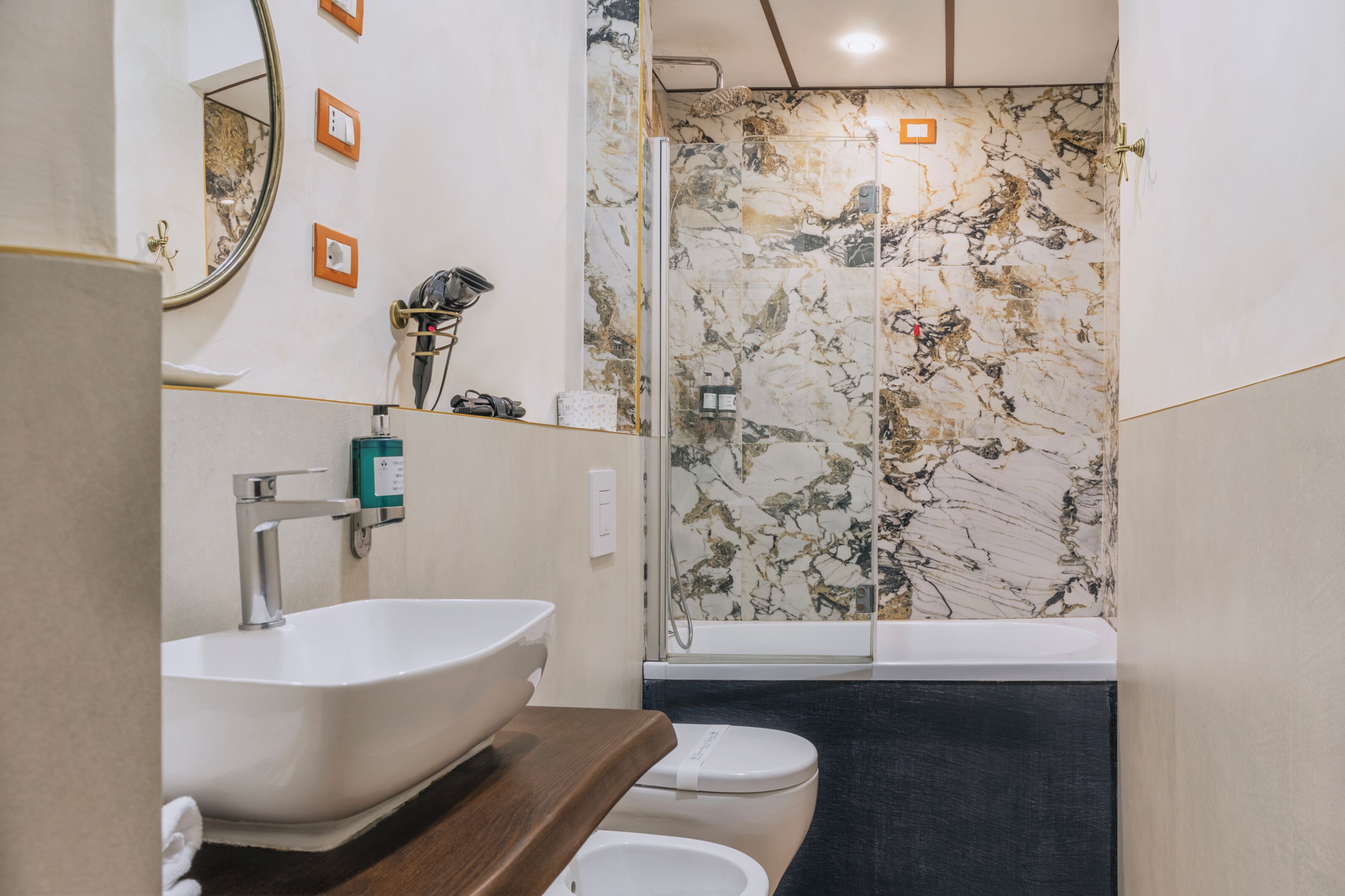 A bathroom with a white sink, a toilet, and a shower with marble walls.