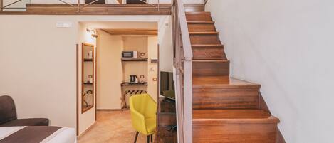 A hotel room with a wooden staircase, a bed, a yellow chair, and a kitchenette area.