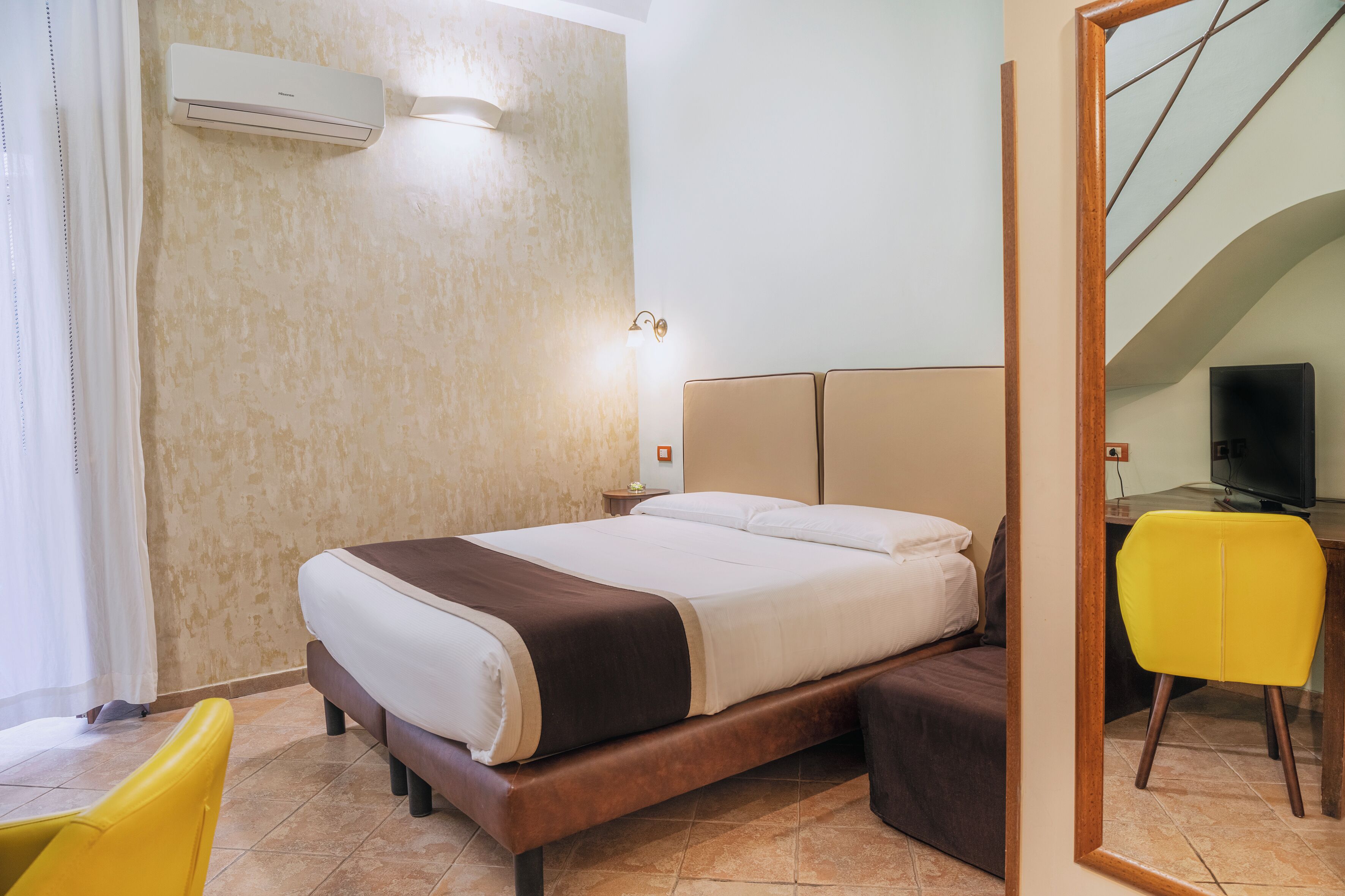 Habitación de hotel con cama, escritorio con silla, aire acondicionado y lámpara de pared.