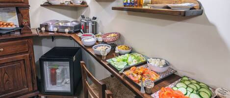 Una mesa de buffet con diferentes alimentos, un refrigerador y estantes con condimentos.