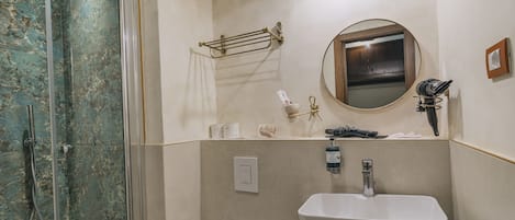 Un baño con cabina de ducha de vidrio, un lavamanos blanco, un espejo y un perchero para toallas.