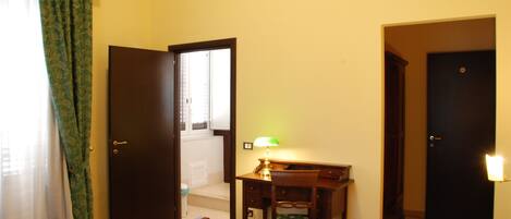 Una habitación de hotel con cama, escritorio, silla, lámpara y puerta que da a una escalera.
