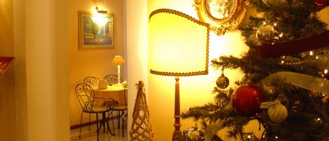 A warmly lit room with a Christmas tree, a dining table with chairs, and a lamp.