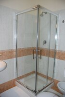 Un box de ducha con paredes de vidrio, un cabezal de ducha manual, un lavamanos blanco y un inodoro.
