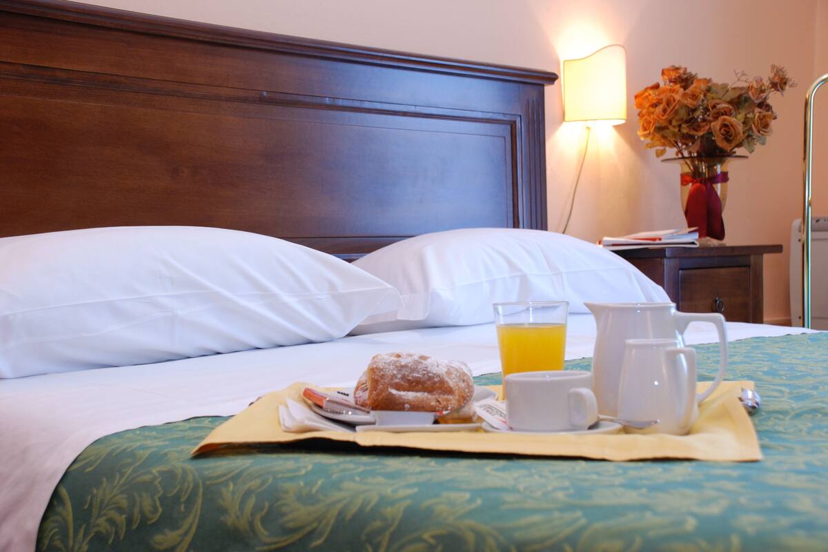 A neatly made bed with white linens, a breakfast tray with a croissant, coffee cups, and a glass of orange juice.