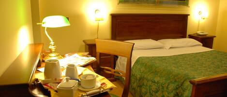 A hotel room with a bed, bedside table, lamp, and a tray with cups and a teapot.