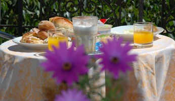 Una tavola imbandita con prodotti per la colazione, tra cui pasticcini, un bicchiere di latte e succo d'arancia, circondata da fiori viola.