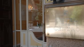 L’entrée d’un hôtel, avec une porte en verre, une plaque en laiton portant l’inscription « Hôtel Del Centro » et le numéro « 72 » au-dessus de la porte.