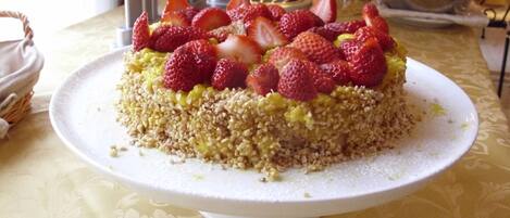 A cake with strawberries on a white plate on a table with a patterned tablecloth.
