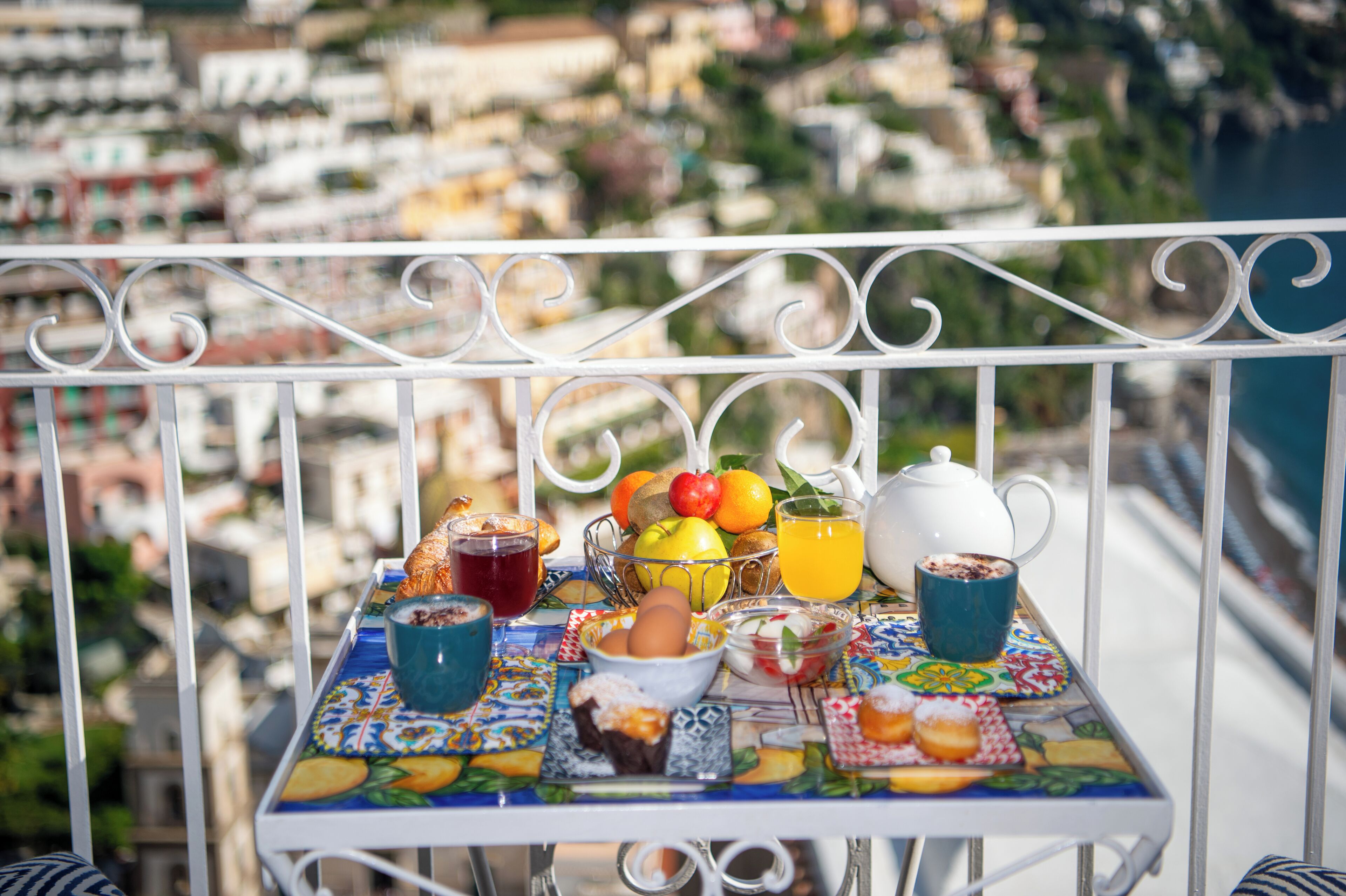 Une table sur un balcon, avec des aliments pour le petit-déjeuner, une vue sur le paysage urbain et une rambarde.