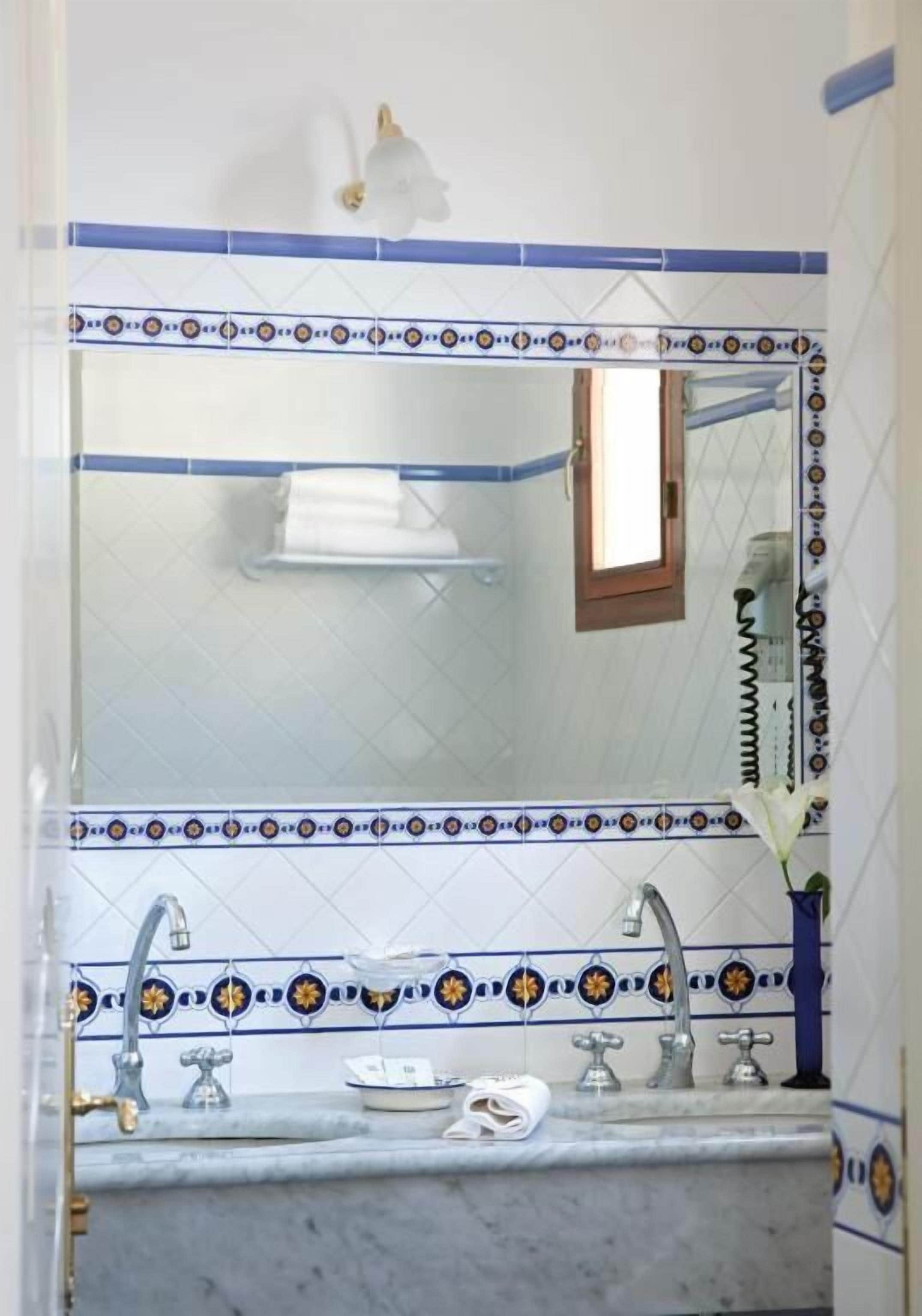 A bathroom with a tiled backsplash, a mirror, a sink with two faucets, and a towel rack.