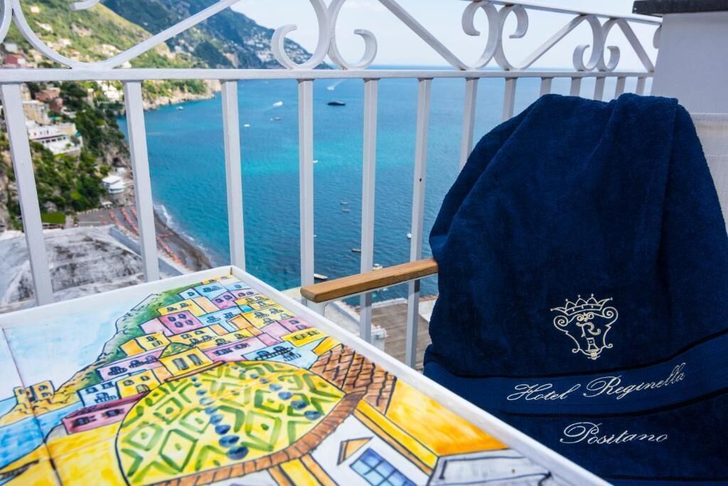 A balcony with a view of the sea, a colorful tiled floor, and a towel with "Hotel Reginello Postano" embroidered on it.