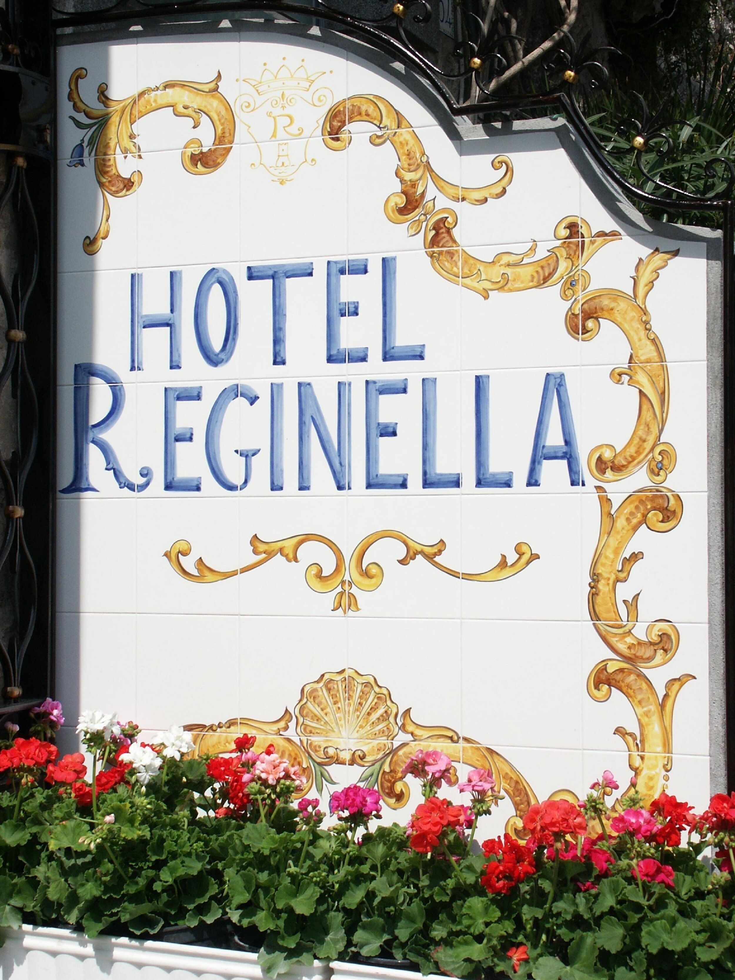 A sign for Hotel Regina with decorative gold and blue lettering, surrounded by vibrant flowers.