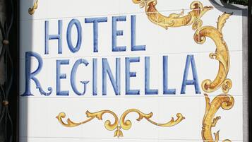 A sign for Hotel Regina with decorative gold and blue lettering, surrounded by vibrant flowers.