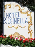 A sign for Hotel Regina with decorative gold and blue lettering, surrounded by vibrant flowers.